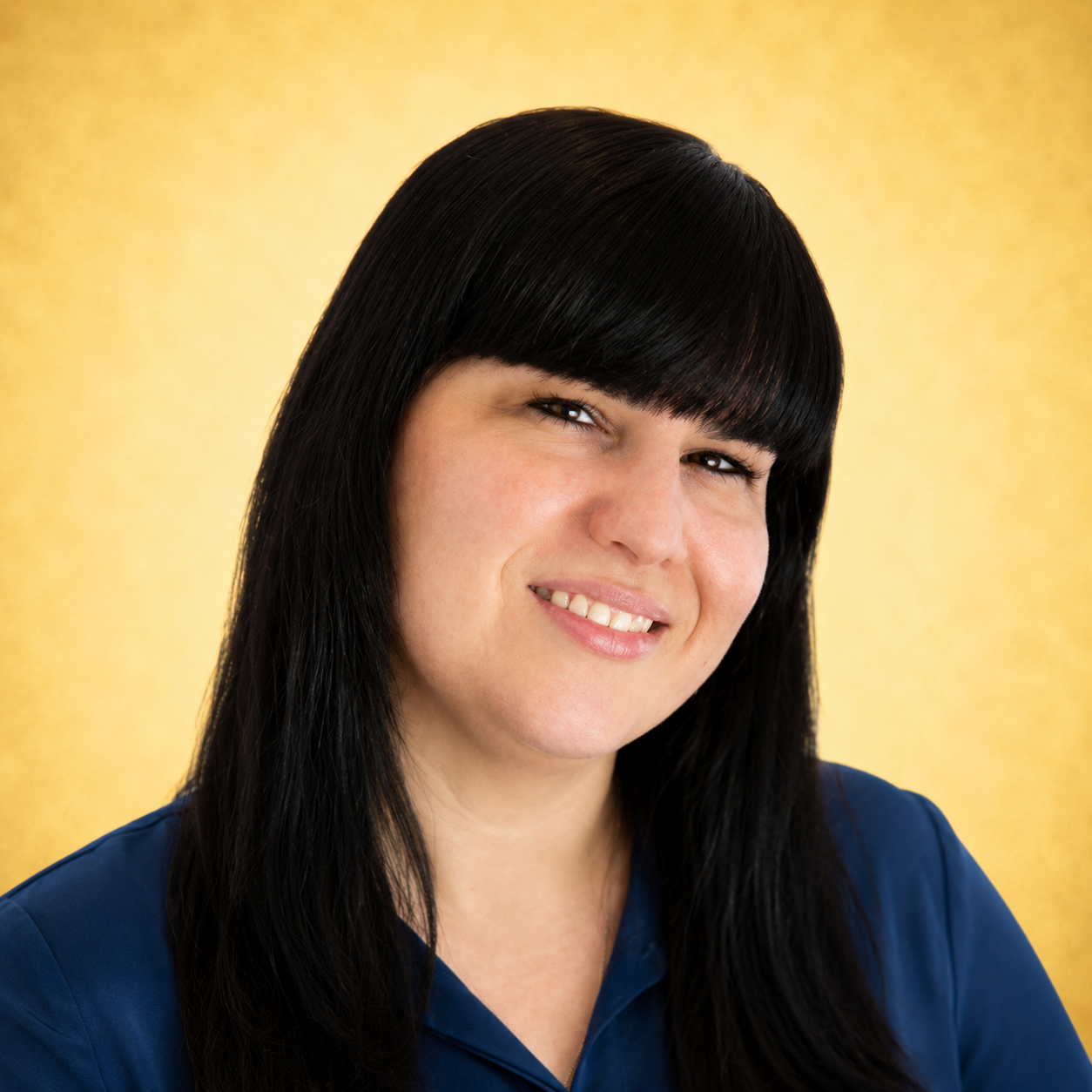 A woman smiling against a yellow background, wearing a blue top.