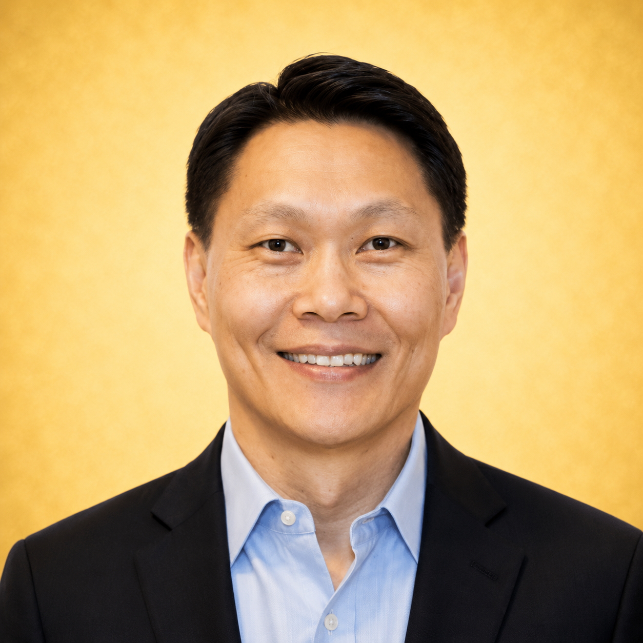 A person smiling in a formal suit with a golden background.