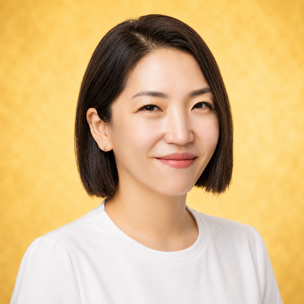A woman with short hair smiles against a gold background.