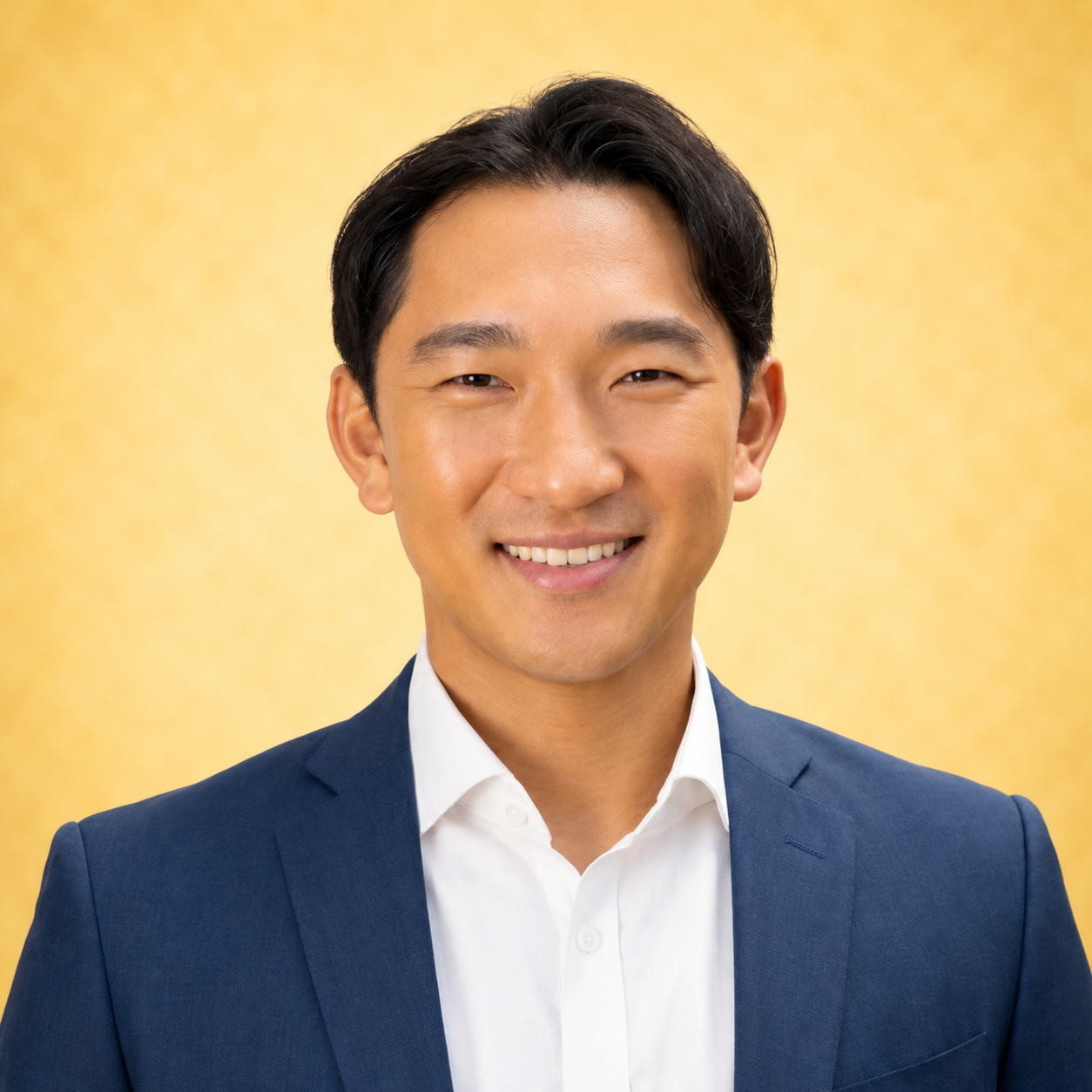 A man in a blue suit smiling against a yellow background.