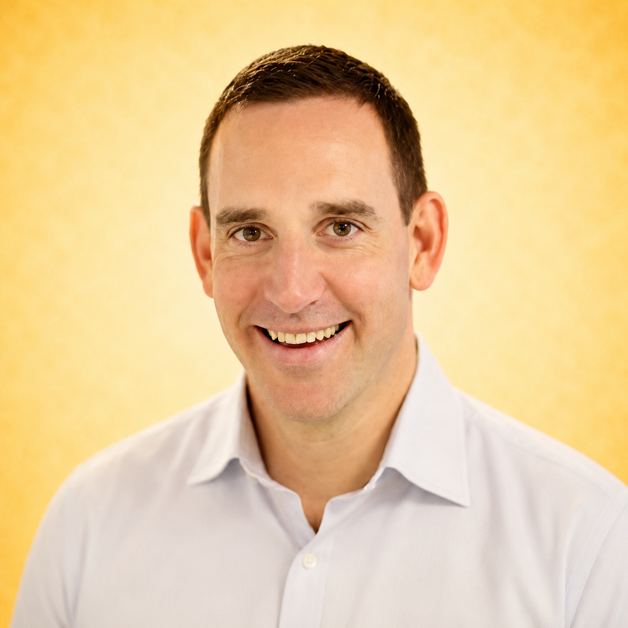 A smiling man in a white shirt against a yellow background.