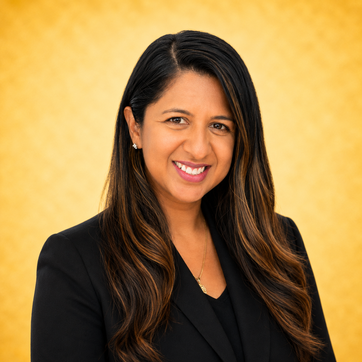 A woman in a black blazer smiling against a gold background.