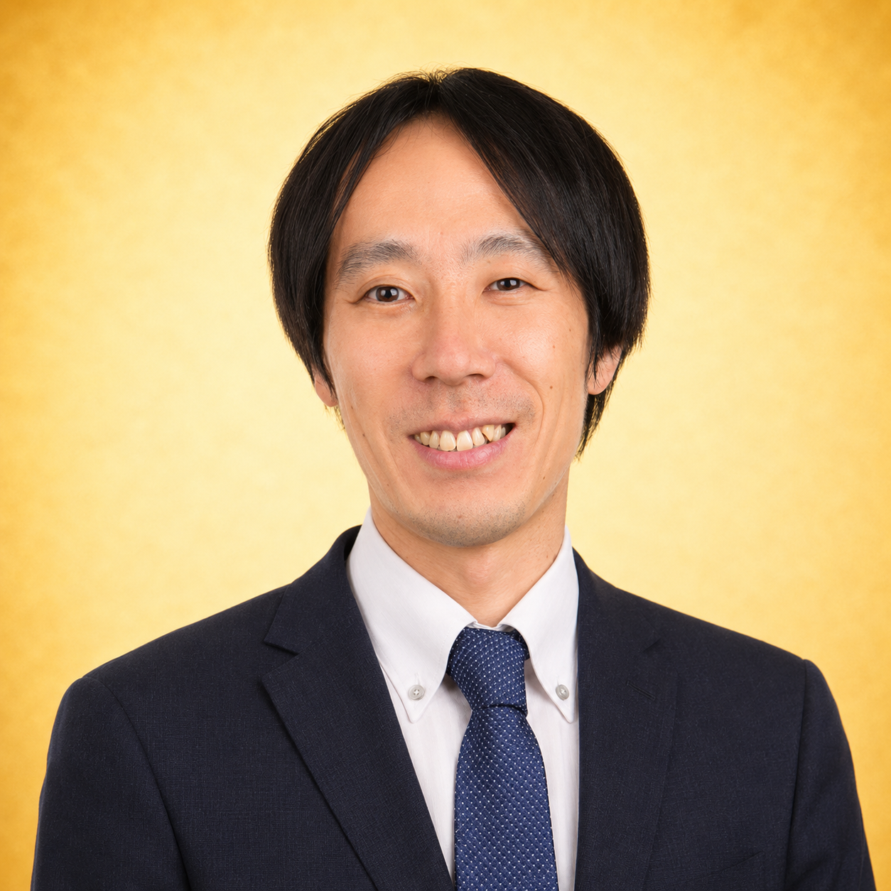 Man in a suit smiling against a yellow background.