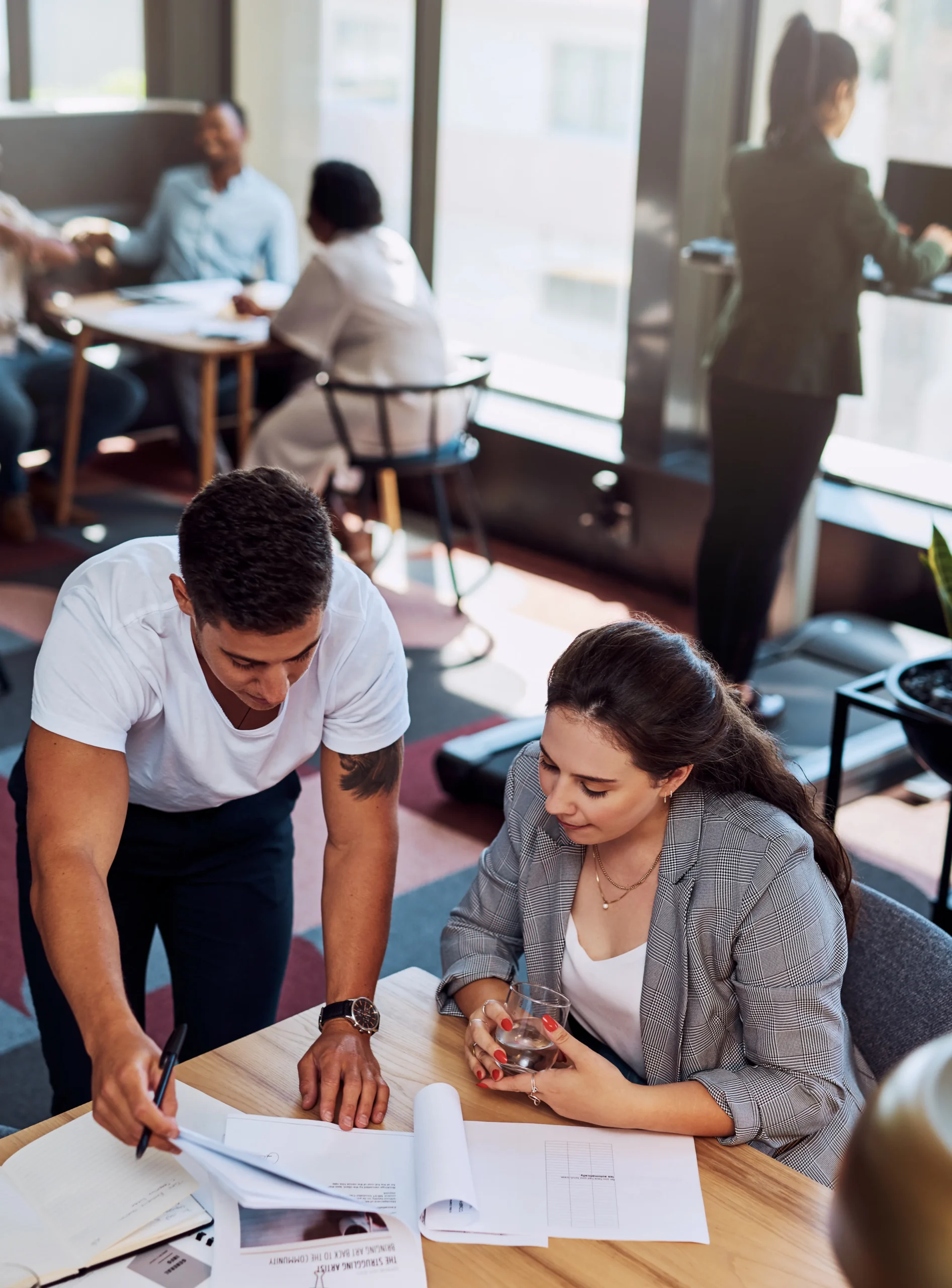 A man and a woman collaborating over documents at an office table, reviewing plans and notes.
