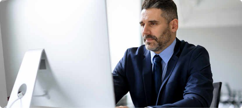 A professional man in a suit working on a desktop computer in a bright modern office.