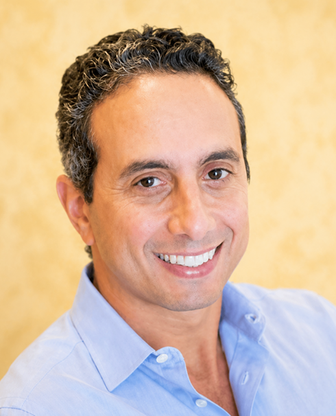 Smiling professional man headshot in a light blue shirt with warm beige background