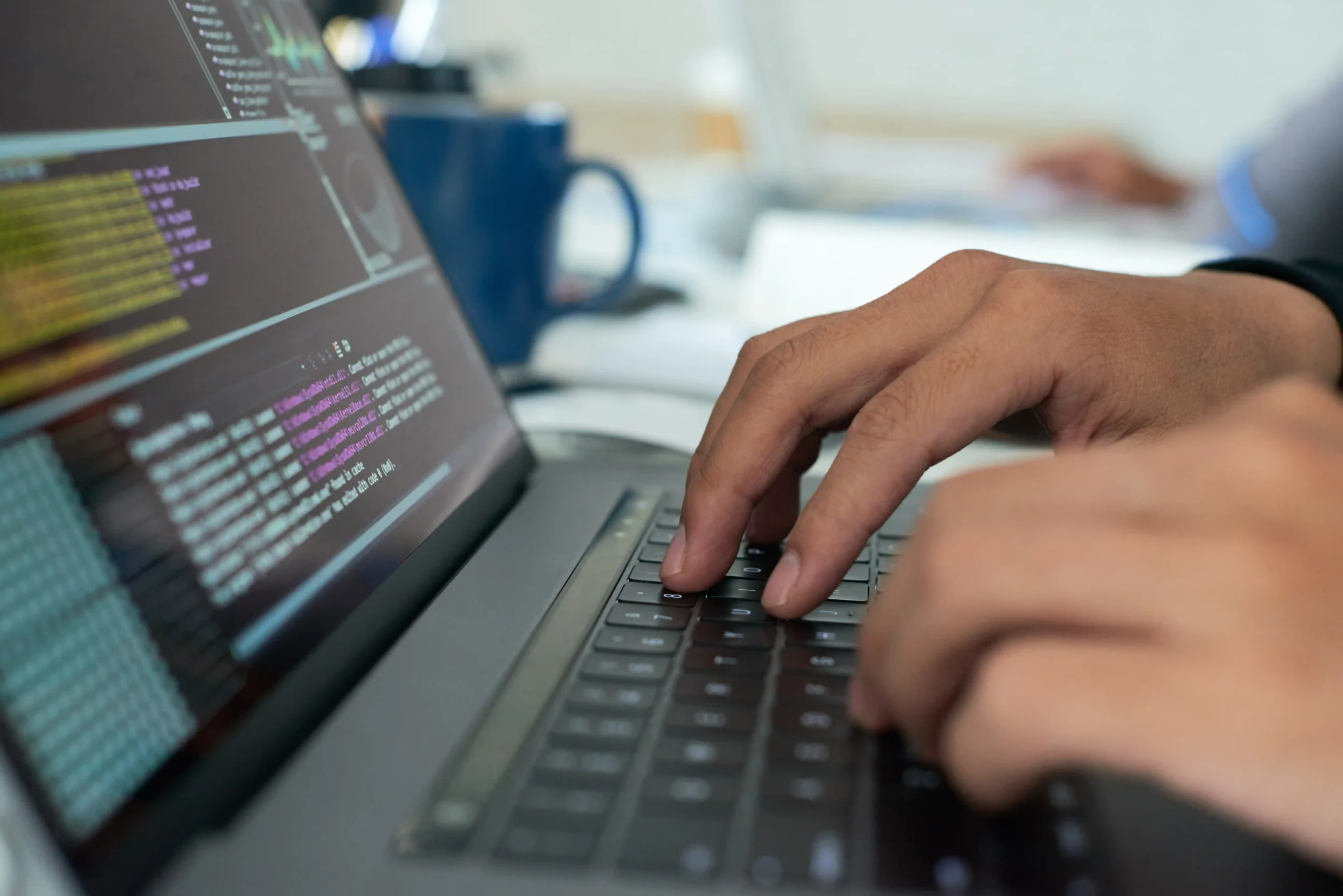 Person typing code on a laptop keyboard, terminal code visible on screen and a coffee mug in background.