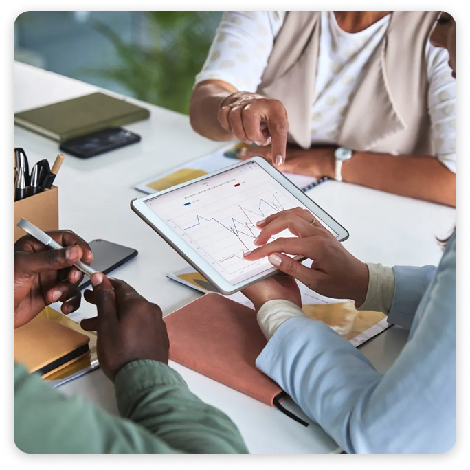 Three people pointing at line charts on a tablet during a business meeting