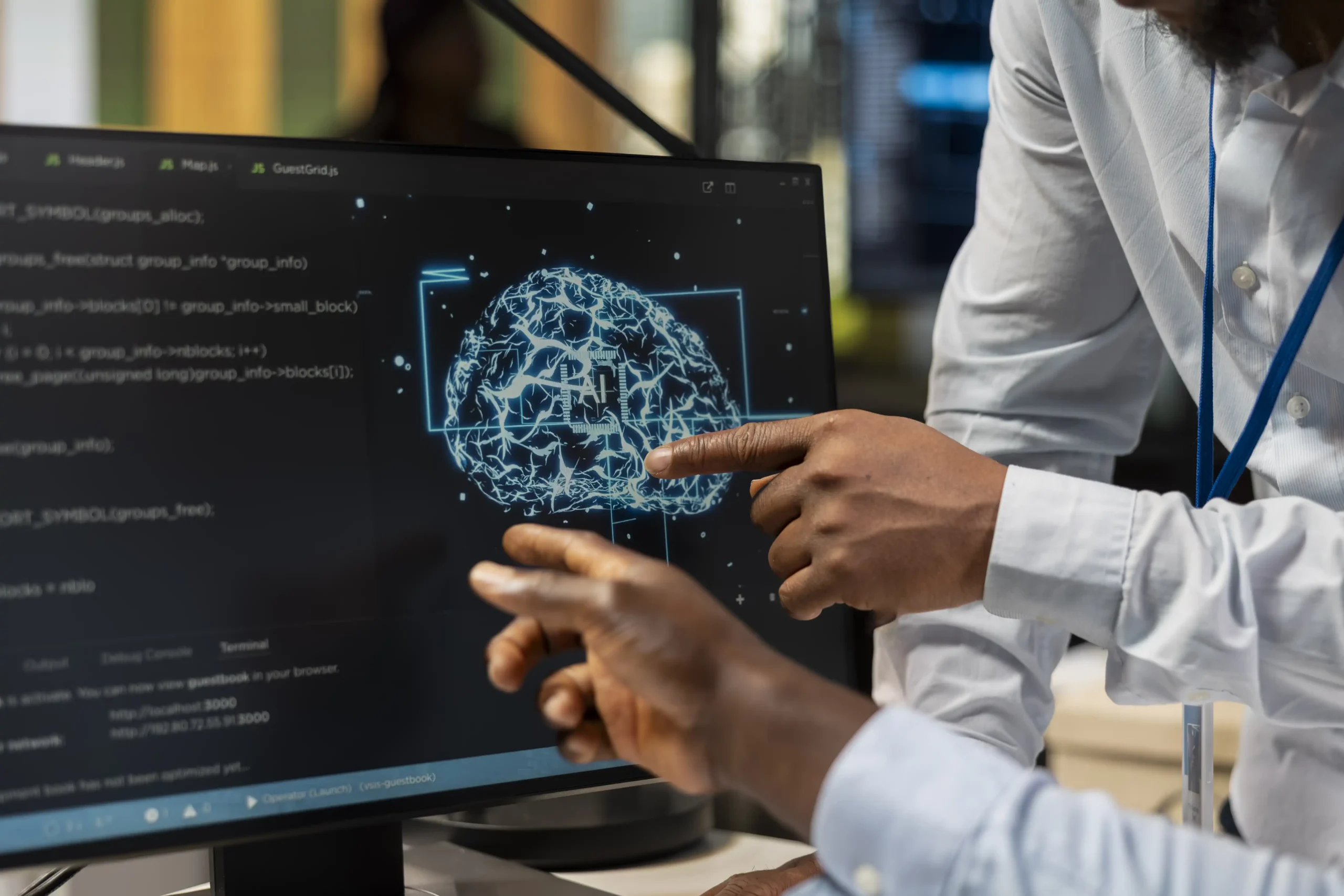 Two people pointing at a computer monitor displaying an AI neural-network brain graphic with code on screen
