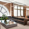 Modern office lounge with arched window, exposed brick wall, sectional sofas and a low coffee table with plant.