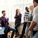 Five coworkers smiling and talking in a bright modern office with large windows
